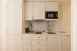 Cozinha com armários brancos, micro-ondas preto, painel de fundo de mármore e pia de aço inoxidável.