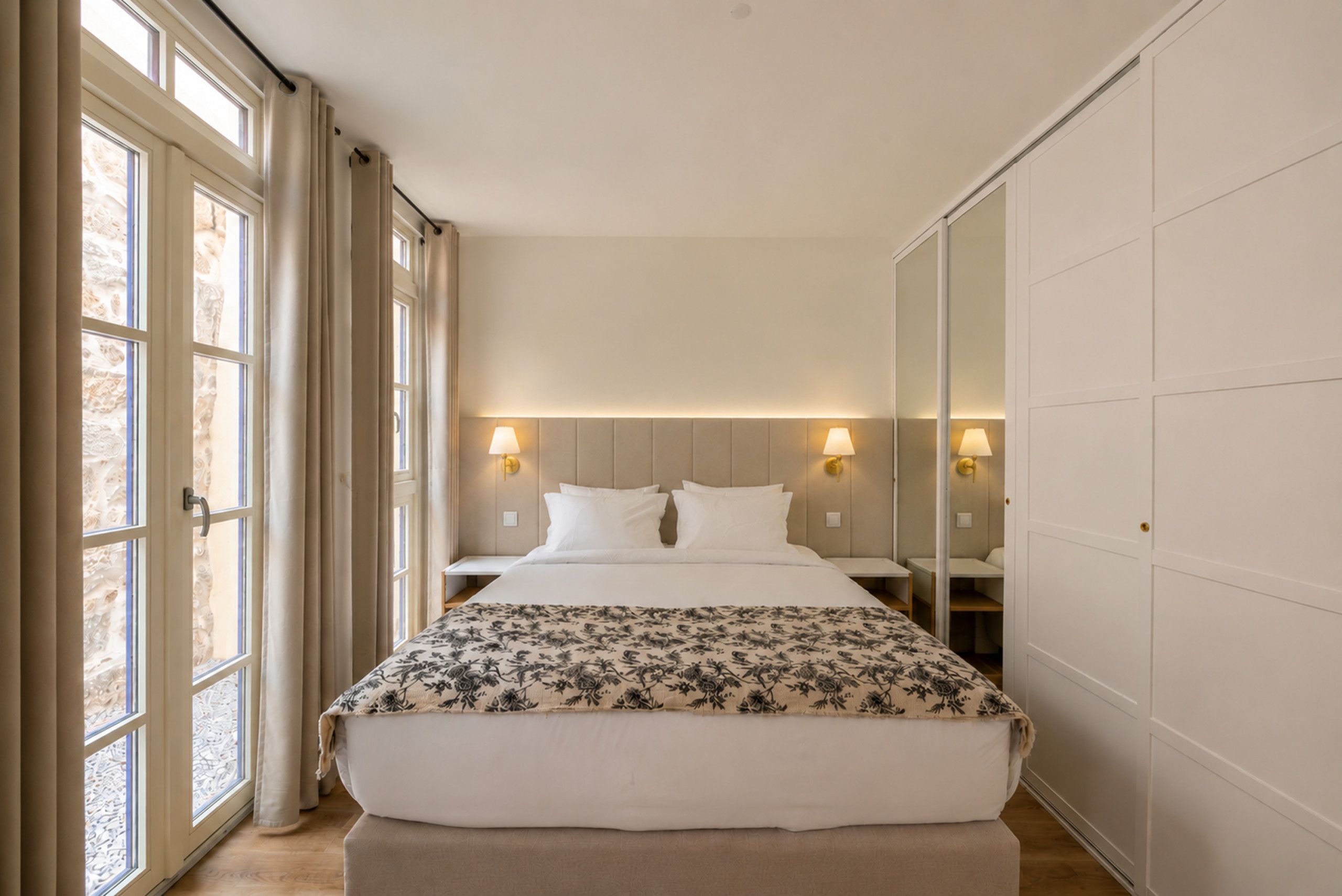 A hotel room with a large bed, bedside lamps, a wardrobe, and a window with curtains.