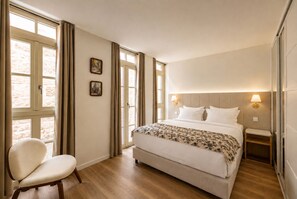 Quarto de hotel com cama, cadeira, mesa de cabeceira e janela com cortinas.
