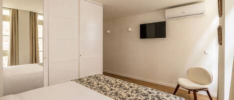 A bedroom with a bed, a wardrobe, a chair, a television, and an air conditioning unit.