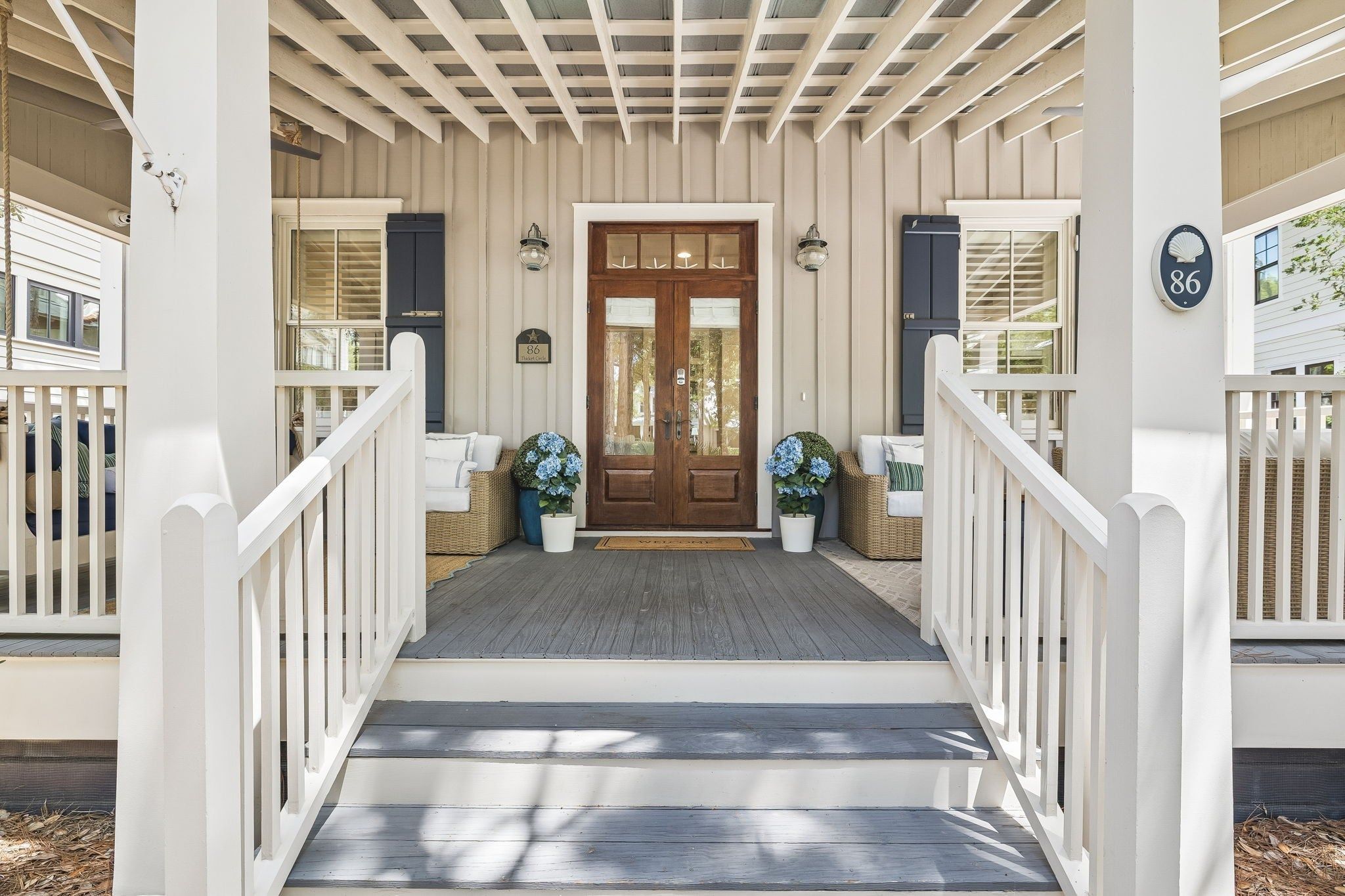A wooden front porch with a double door, white railings, and potted plants.