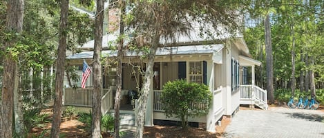 A two-story house with a porch, surrounded by trees.