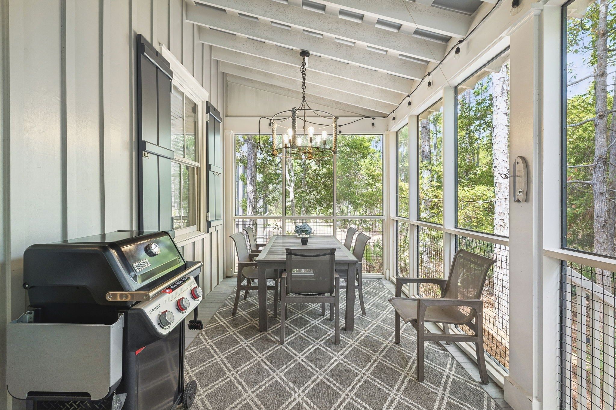 Une terrasse couverte avec un barbecue, une table, des chaises et une vue sur les arbres.