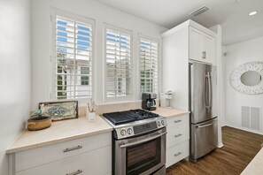 Eine moderne Küche mit eingebautem Gaskochfeld, Edelstahlgeräten und einem großen Fenster mit Jalousien.