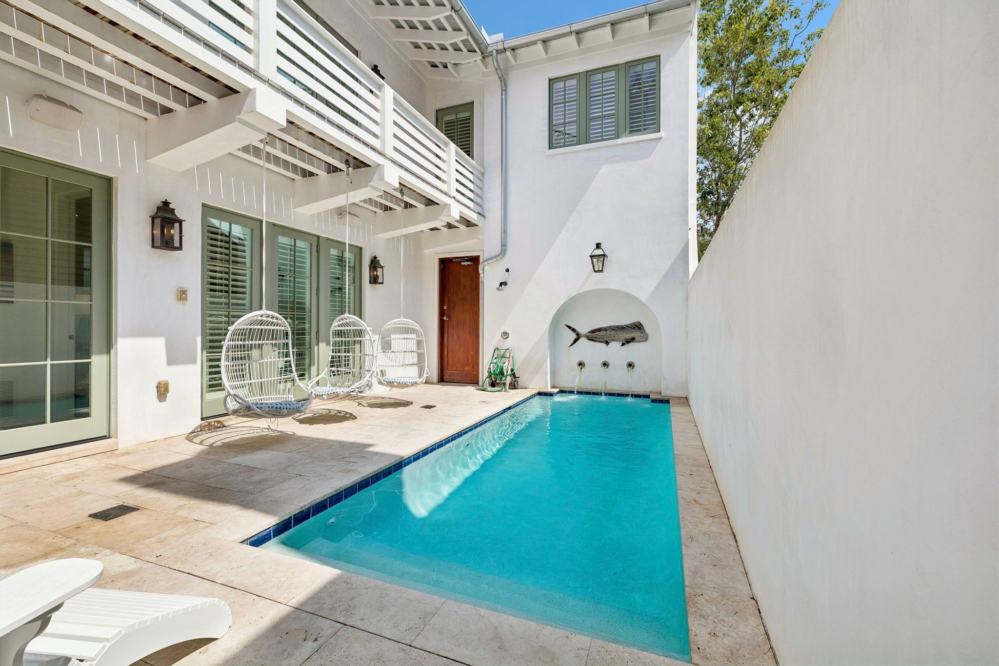 A swimming pool with a clear blue water feature, surrounded by a white building with a balcony and outdoor seating.