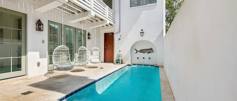 A swimming pool with a clear blue water feature, surrounded by a white building with a balcony and outdoor seating.