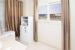 A room with a bed, a small table, a white cabinet, a window with curtains, and a refrigerator. - Gem View Inn (Giza Governorate,)