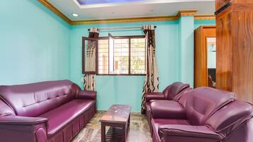 A room with teal walls, two purple leather sofas, a wooden coffee table, and a window with curtains.