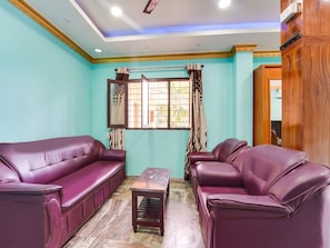 A room with teal walls, two purple leather sofas, a wooden coffee table, and a window with curtains.