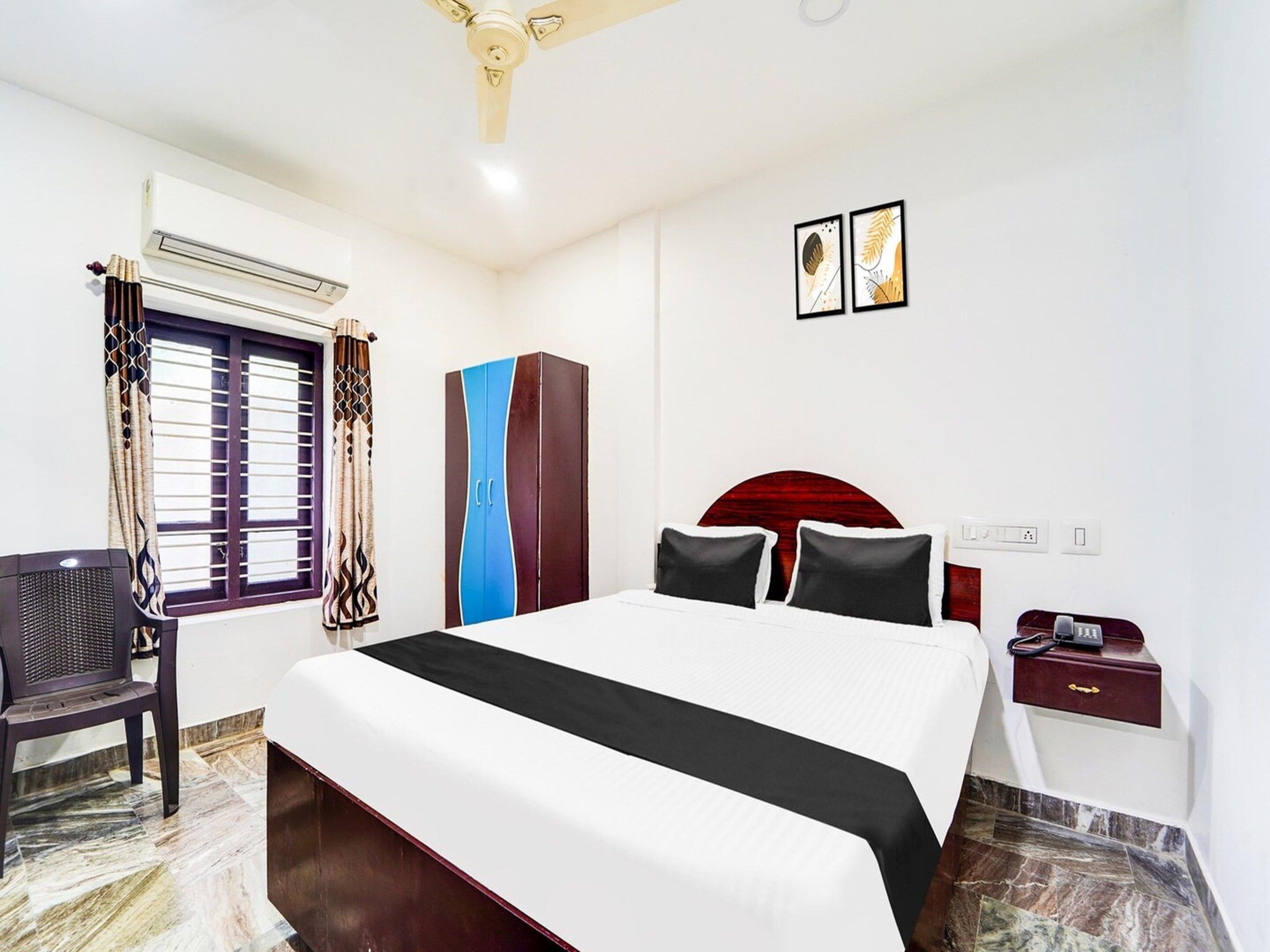 A hotel room with a bed, a desk, a chair, a wardrobe, and a ceiling fan.