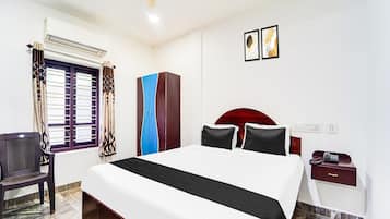 A hotel room with a bed, a desk, a chair, a wardrobe, and a ceiling fan.