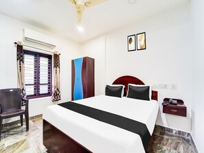 Una habitación de hotel con cama, escritorio, silla, armario y ventilador de techo.