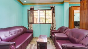 Um quarto com dois sofás de couro roxo, uma mesa de centro de madeira e uma janela com cortinas estampadas.