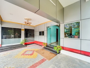 A modern building entrance with a tiled floor, a 'Welcome' sign, and potted plants.