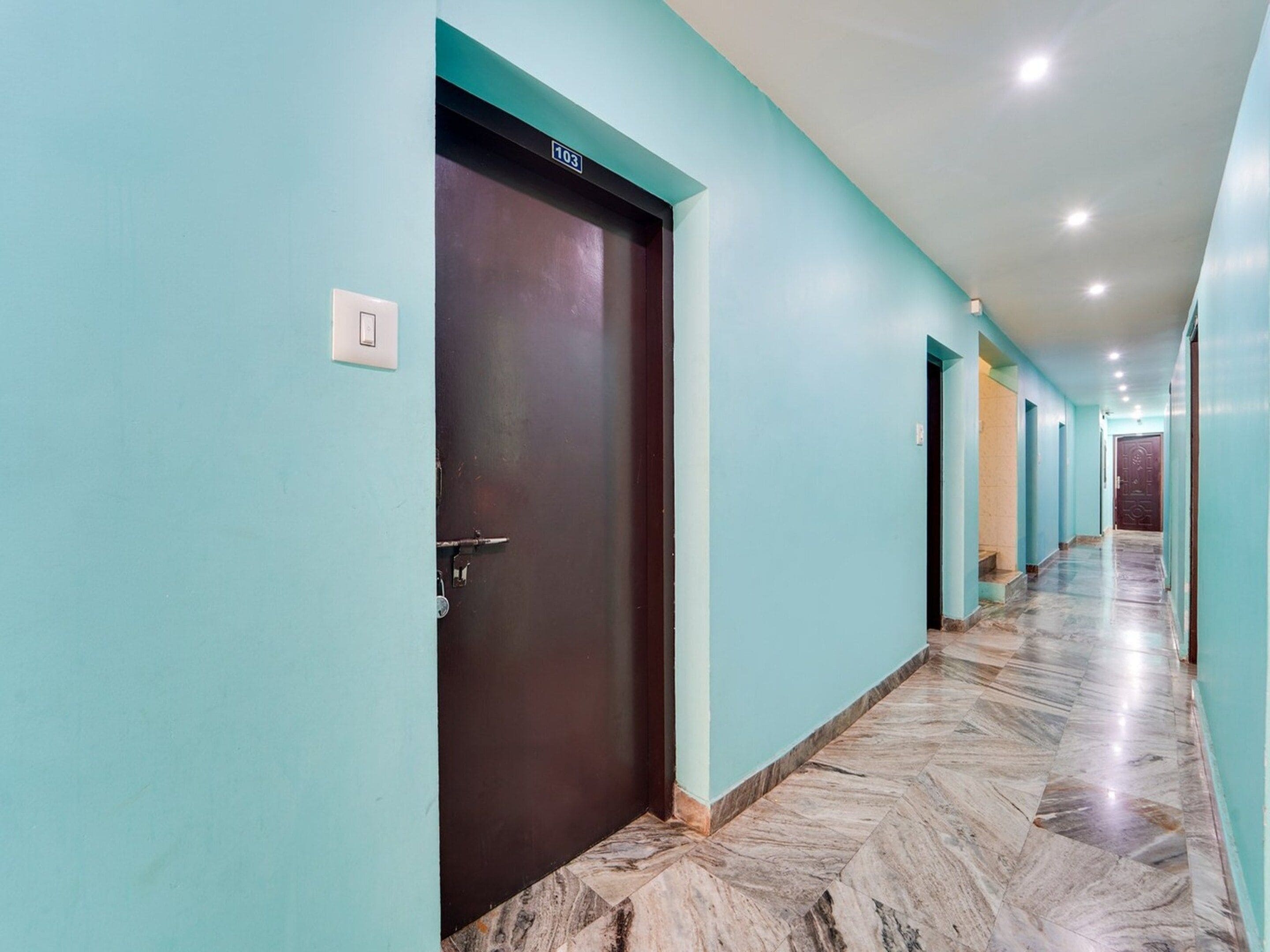 A hallway with teal walls, a marble floor, and a dark brown door marked with the number 103.