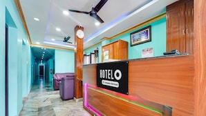 Uma área de recepção de hotel com um balcão de madeira, um relógio e um ventilador de teto.