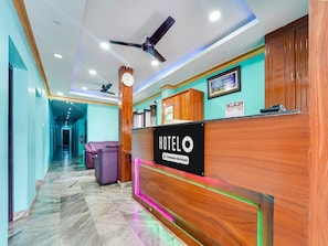 A hotel reception area with a wooden reception desk, a clock, and a ceiling fan. - Deluxe Hotel Jaisas Paradise (Nagercoil)