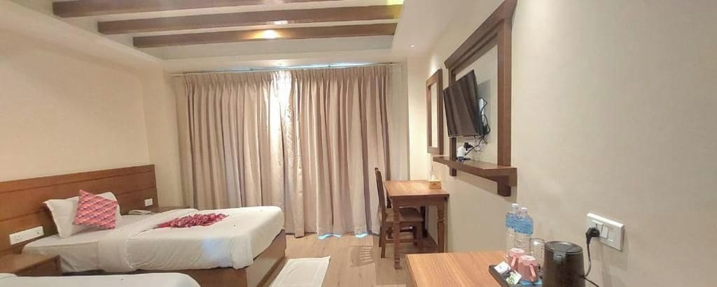 Habitación de hotel con dos camas, un escritorio, una silla, un televisor y una ventana con cortinas.