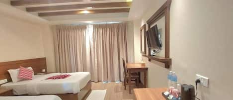 A hotel room with two beds, a desk, a chair, a TV, and a window with curtains.