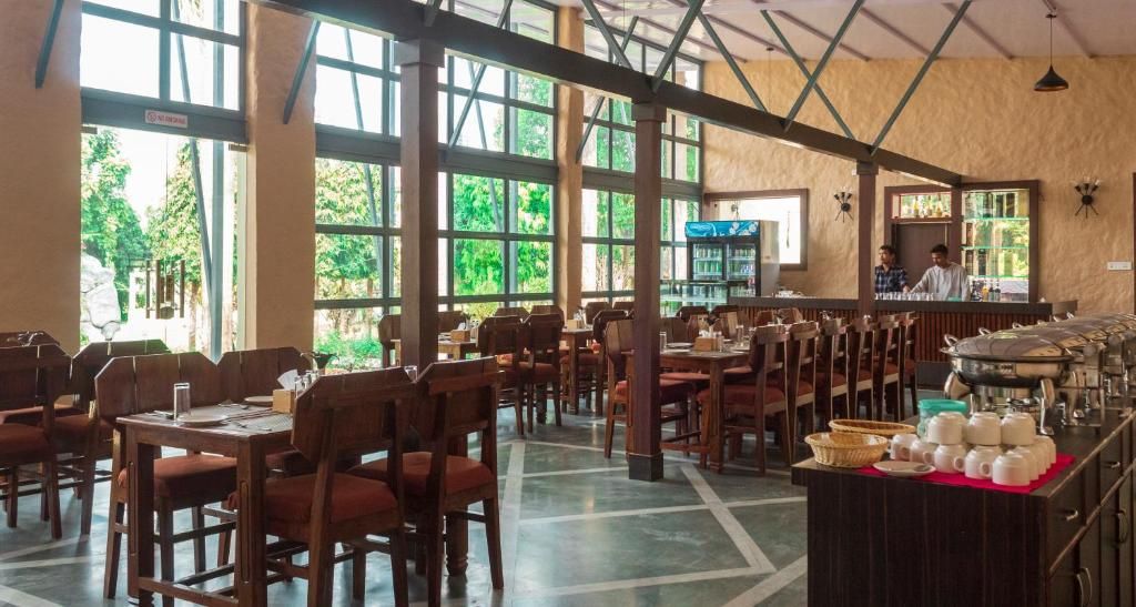 A spacious restaurant with high ceilings and large windows, wooden tables and chairs, and a bar area.