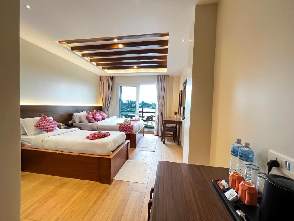 A hotel room with two beds, a dining table, a kitchen area, and a view of the outdoors.