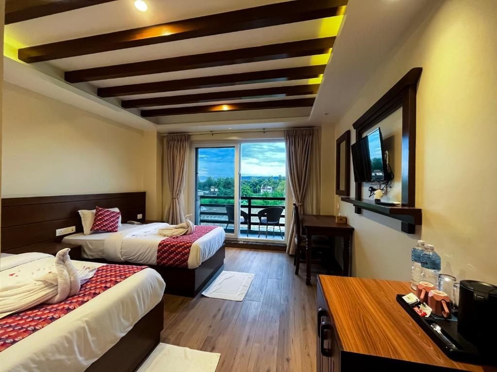 Habitación de hotel con dos camas, un escritorio, televisión y balcón con vistas.