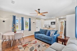 Ein modernes Wohnzimmer mit einem blauen Sofa, einem Esstisch mit Stühlen und einer Küche im Hintergrund.