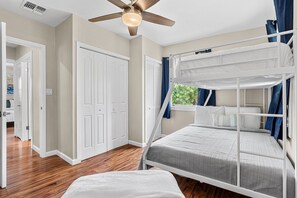 Ein Schlafraum mit Etagenbetten, Deckenventilator, weißen Wänden und Holzboden.