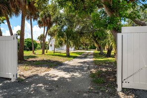 A pathway leading to a gated area with palm trees and a white building. - Family‑Friendly 2BR Beach Home • Walk to Beach & Shops 🌴🏖️ (Cape Canaveral)
