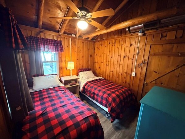 Ein blockhaushaltsähnliches Zimmer mit zwei Betten, einem Deckenventilator und Holzwänden.