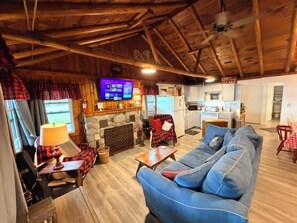 A cozy living room with a stone fireplace, a blue sofa, and a television mounted on the wall. - New!  Chappy's Lakeside Cabin - Lakefront & Comfy!  Includes canoe and kayak! (Oscoda)