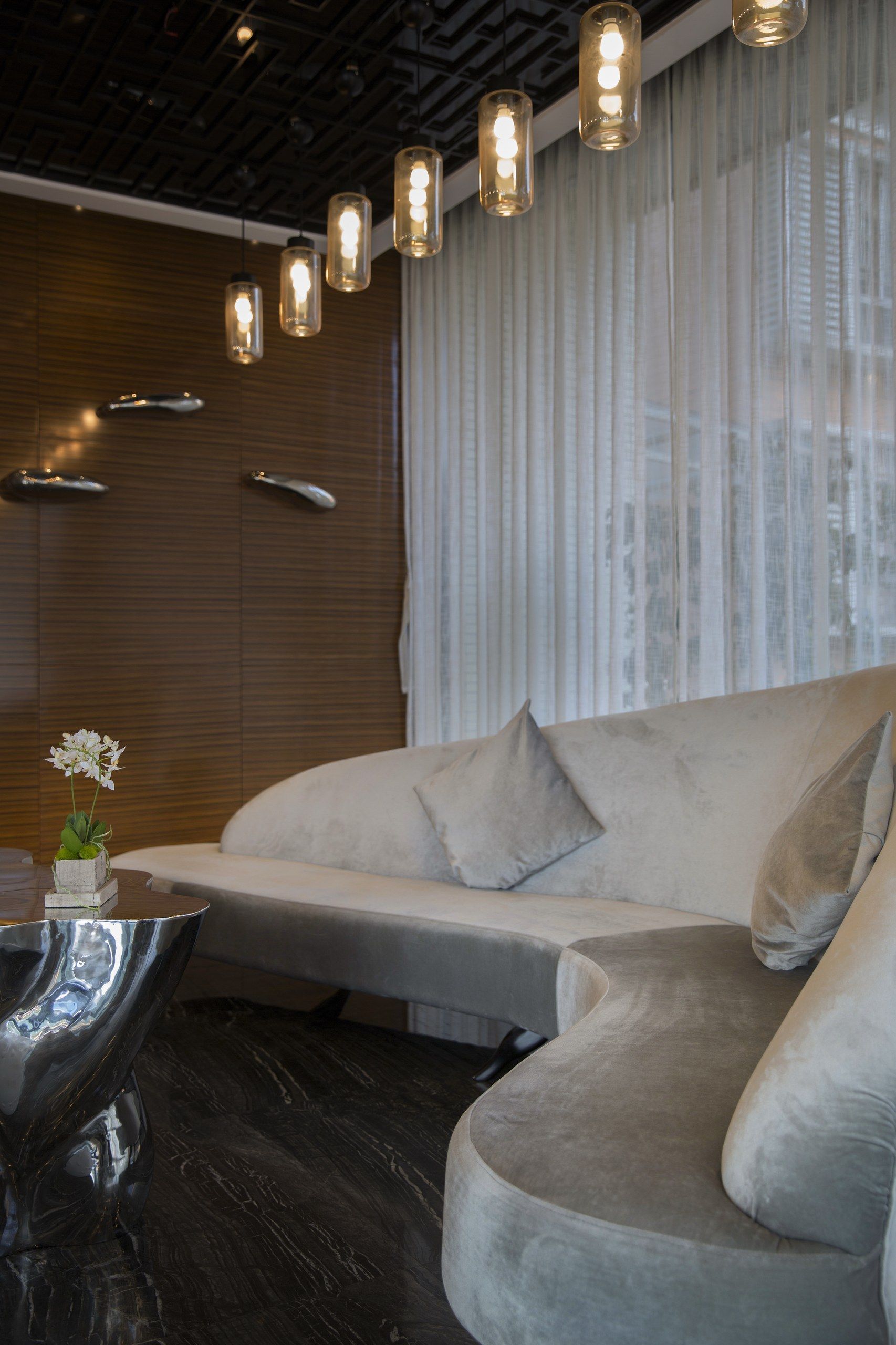 A modern living room with a curved sofa, a reflective coffee table, and pendant lighting.