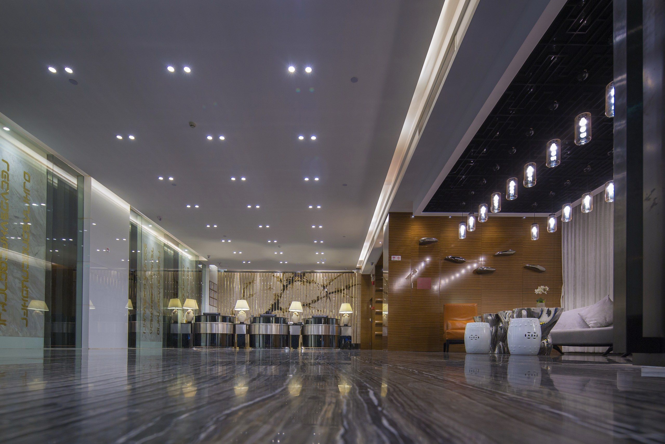 A hotel lobby with a marble floor, a reception desk, and a seating area with a sofa and chairs.
