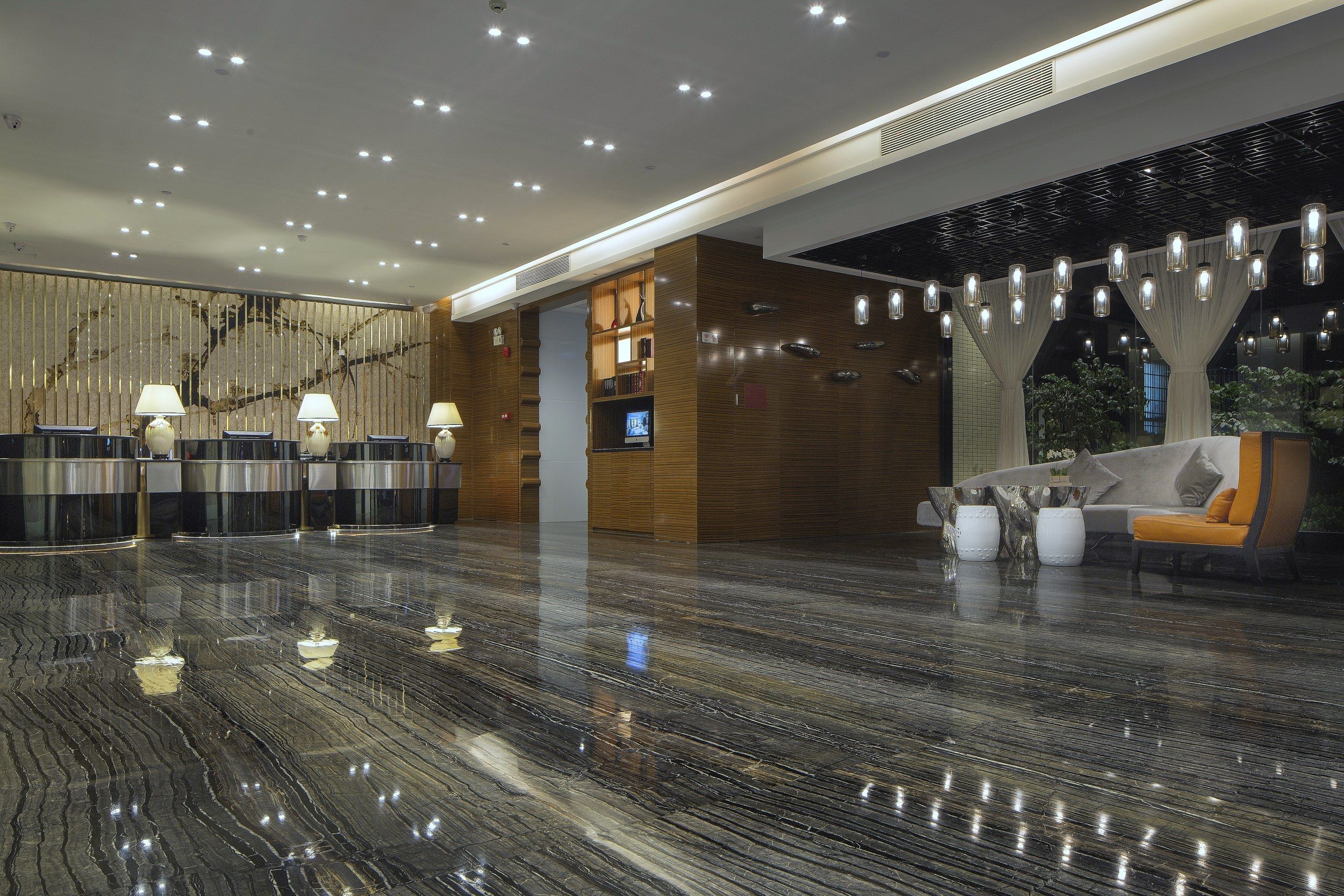 A modern lobby with a marble floor, reception desk, seating area, and decorative lighting.