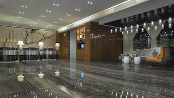 A modern lobby with a marble floor, reception desk, seating area, and decorative lighting.