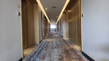 A hotel hallway with a carpeted floor, doors on both sides, and a long corridor leading to a bright end.