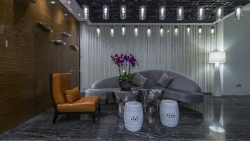 A modern lobby with a leather chair, a sofa, a glass table, and a vase with purple flowers.