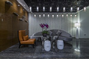 Um lobby moderno com uma poltrona de couro, um sofá, uma mesa de vidro e um vaso com flores roxas.