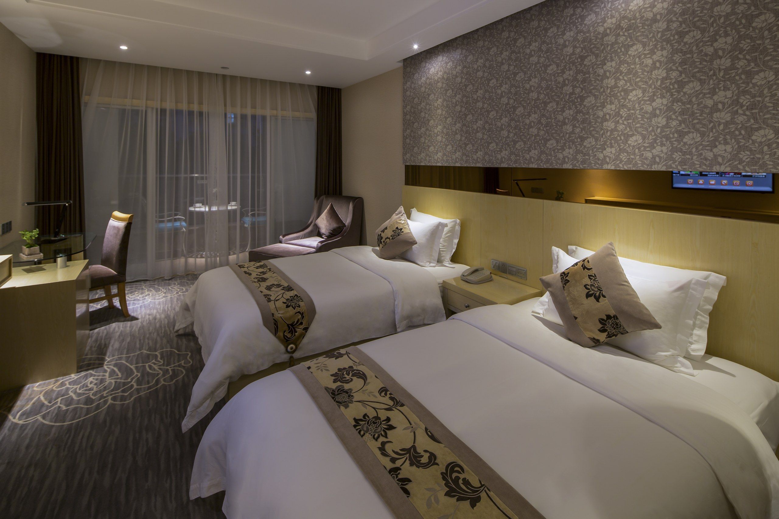 A hotel room with two beds, a desk, a chair, and a television.