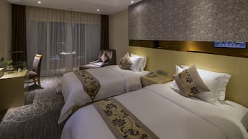 A hotel room with two beds, a desk, a chair, and a television.