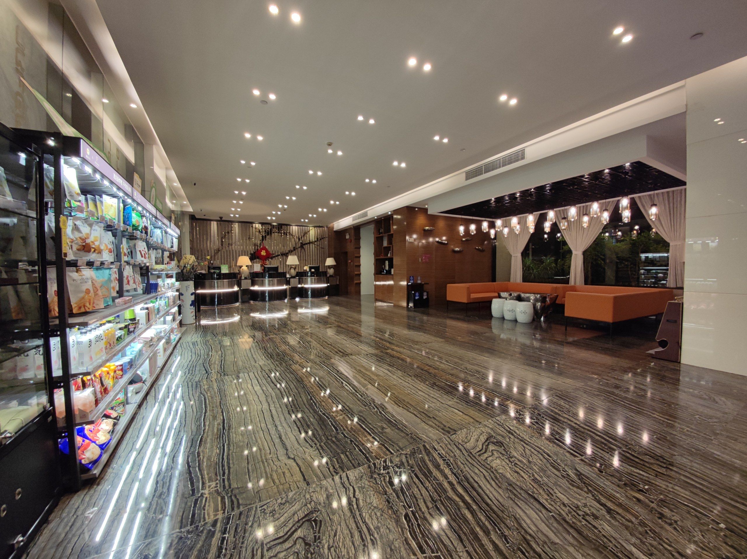 A spacious lobby with a marble floor, a reception desk, and a seating area with a sofa and chairs.