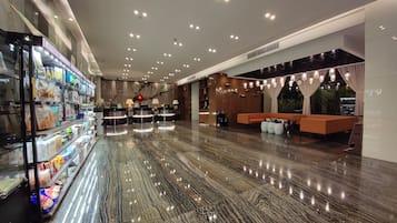 A spacious lobby with a marble floor, a reception desk, and a seating area with a sofa and chairs.