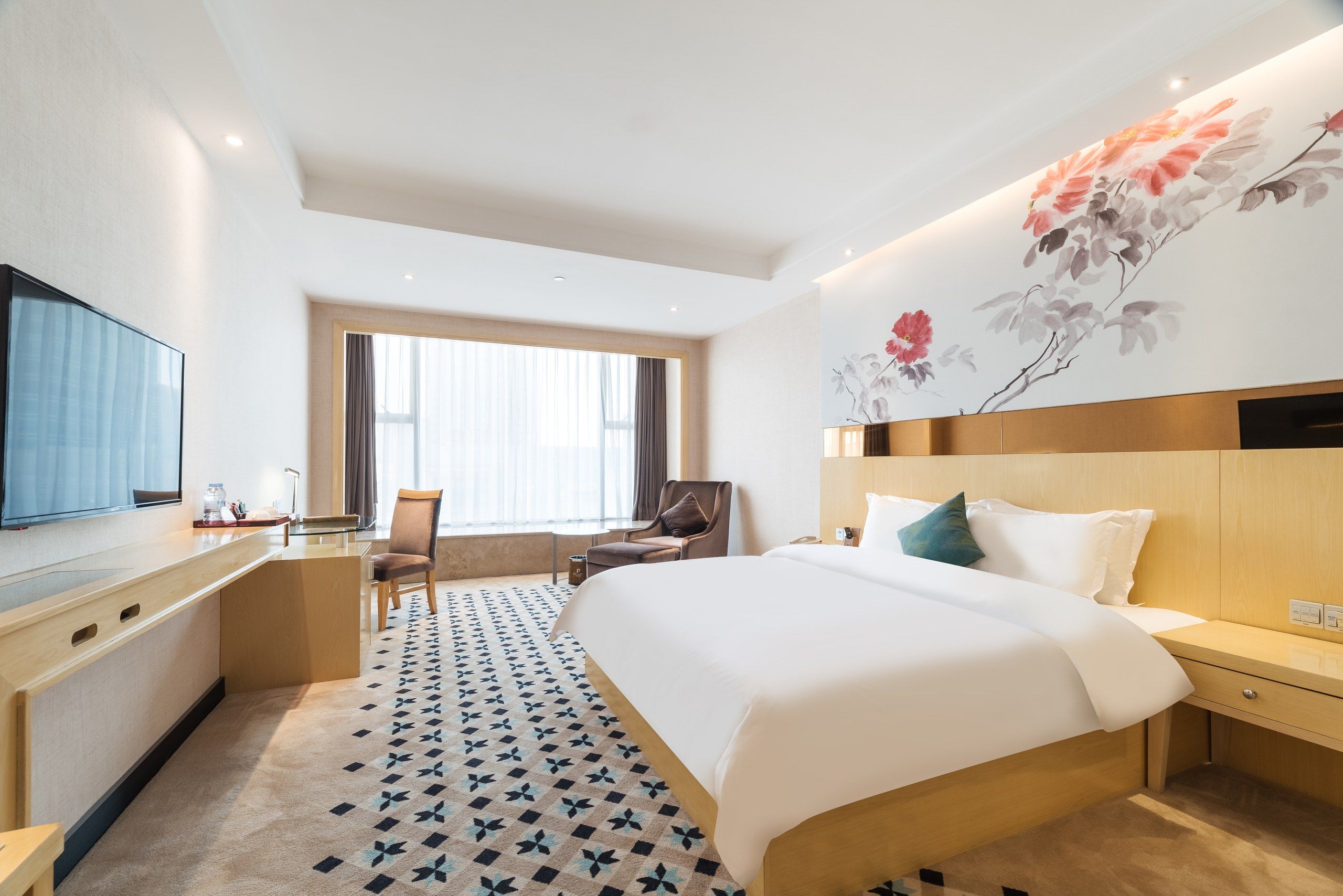 A hotel room with a bed, a desk, a chair, a TV, and a large floral wall mural.