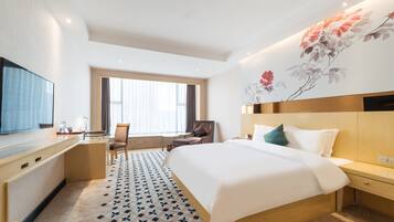 A hotel room with a bed, a desk, a chair, a TV, and a large floral wall mural.