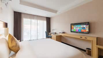 A hotel room with a large bed, a desk, a television, and a window with curtains.