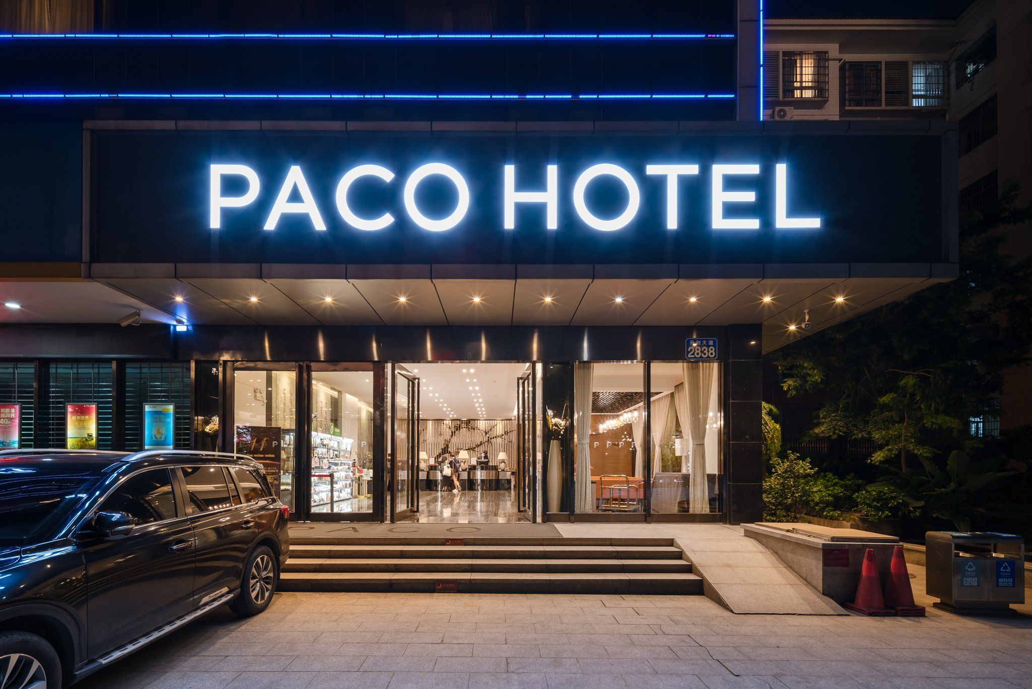 The entrance to a hotel with a prominent sign, a car parked in front, and a staircase leading to the entrance.