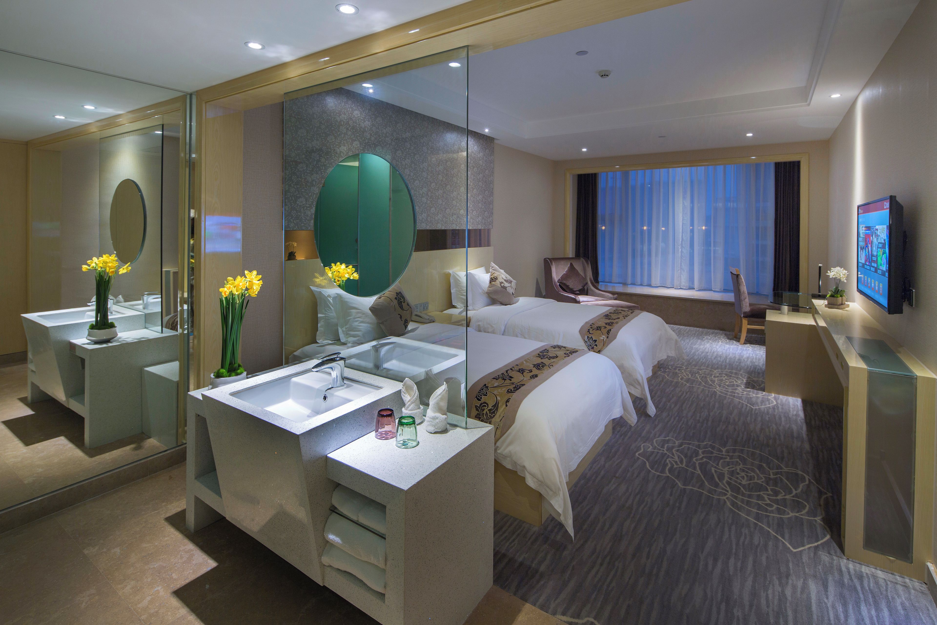 A hotel room with a large bed, a separate sitting area, a bathroom with a vanity, and a television.
