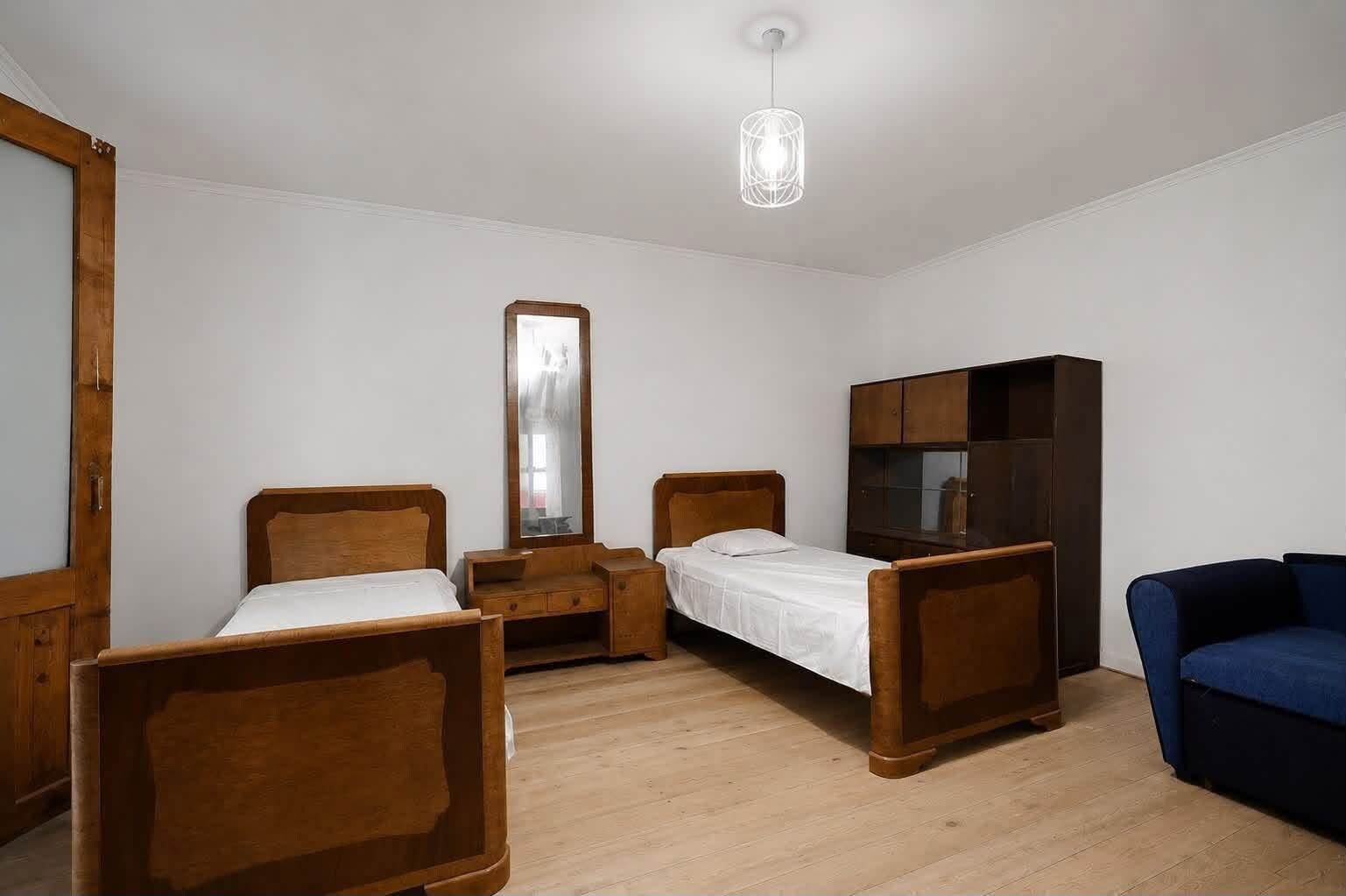 Une chambre avec deux lits en bois, une armoire, un miroir et un luminaire suspendu.