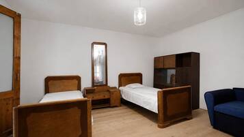 Une chambre avec deux lits en bois, une armoire, un miroir et un luminaire suspendu.