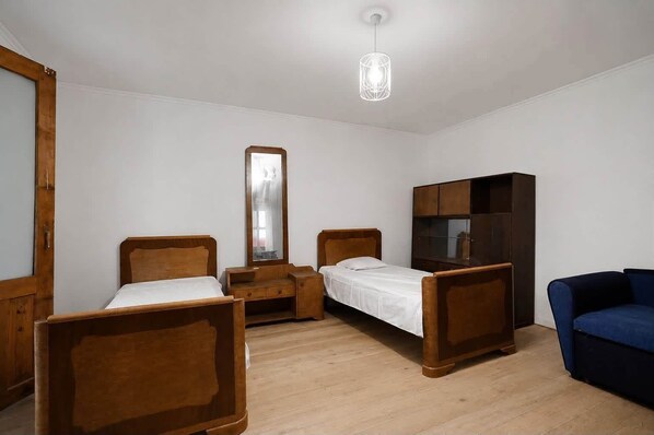 A room with two wooden beds, a wardrobe, a mirror, and a hanging light fixture.